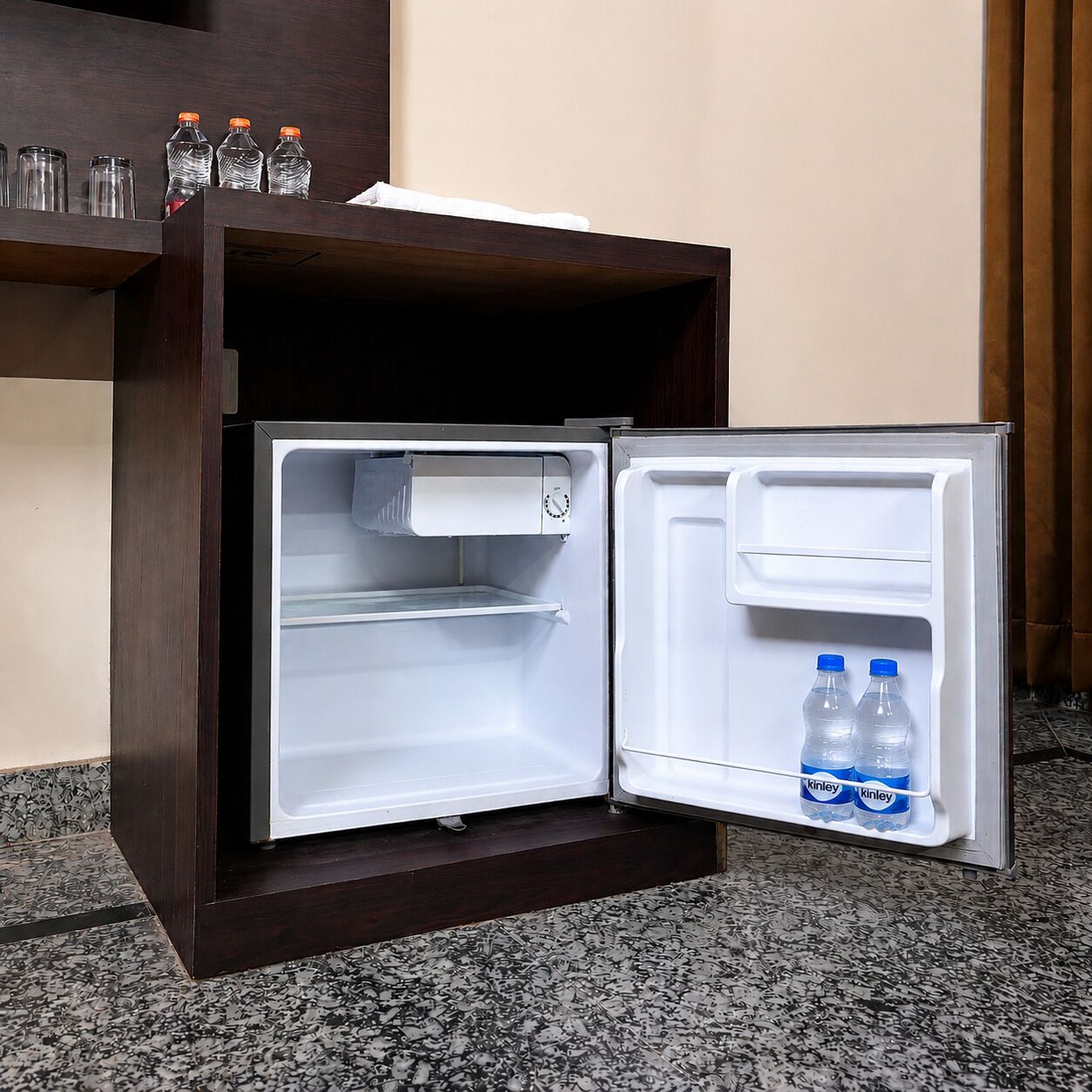 A compact refrigerator with two shelves, one with water bottles and the other empty.