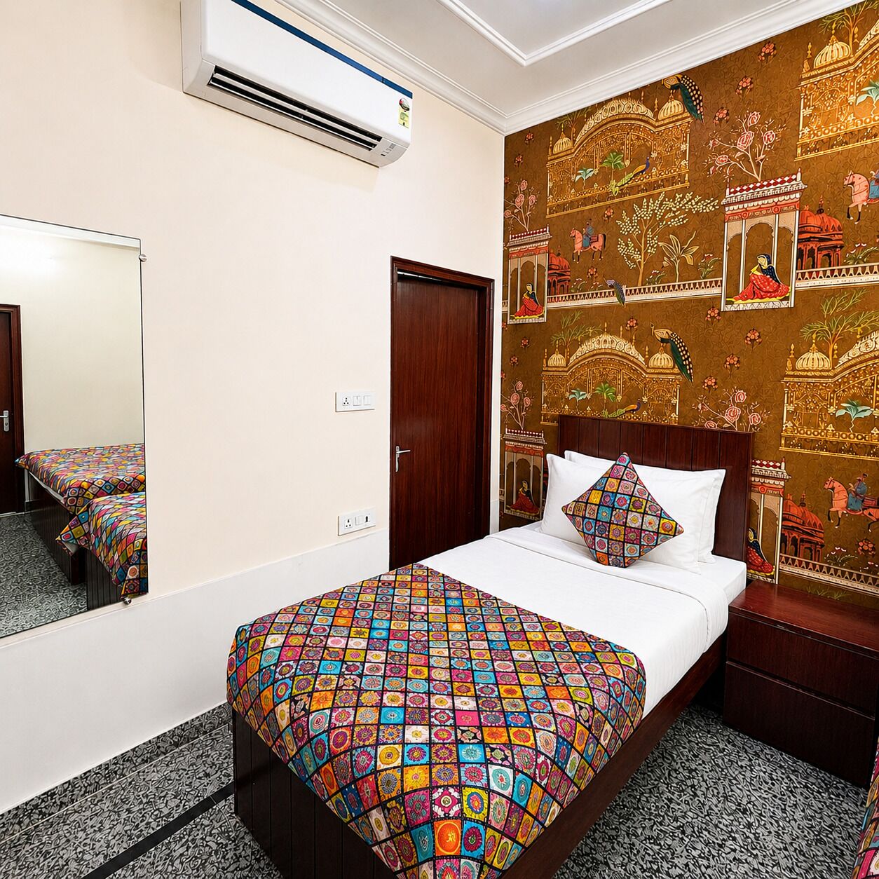 A hotel room with a bed, a mirror, an air conditioner, and a wall with traditional artwork.