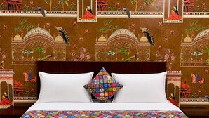 A bed with a colorful quilt, white pillows, and a patterned wall with traditional designs. - The Manthan Stays (Vrindavan)