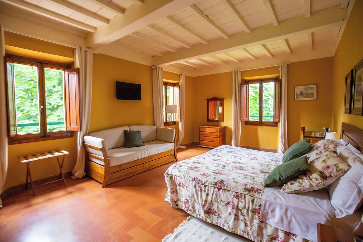 A bedroom with a bed, a sofa, a dresser, and a window.