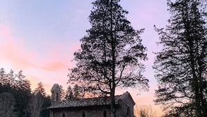 A rustic stone building with a tiled roof, surrounded by a wooden fence and tall trees. - Albergo Villa San Michele  (Greve in Chianti)