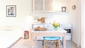 Um quarto acolhedor com uma cama, uma mesinha com uma cesta de frutas, uma cozinha compacta e um quadro na parede.