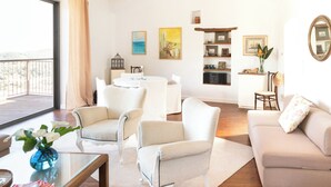 Uma sala de estar espaçosa com varanda, móveis brancos e obras de arte nas paredes.