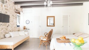 Quarto moderno com parede de pedra, cama de madeira, cadeira de vime e um espaço para café da manhã com pão e frutas.