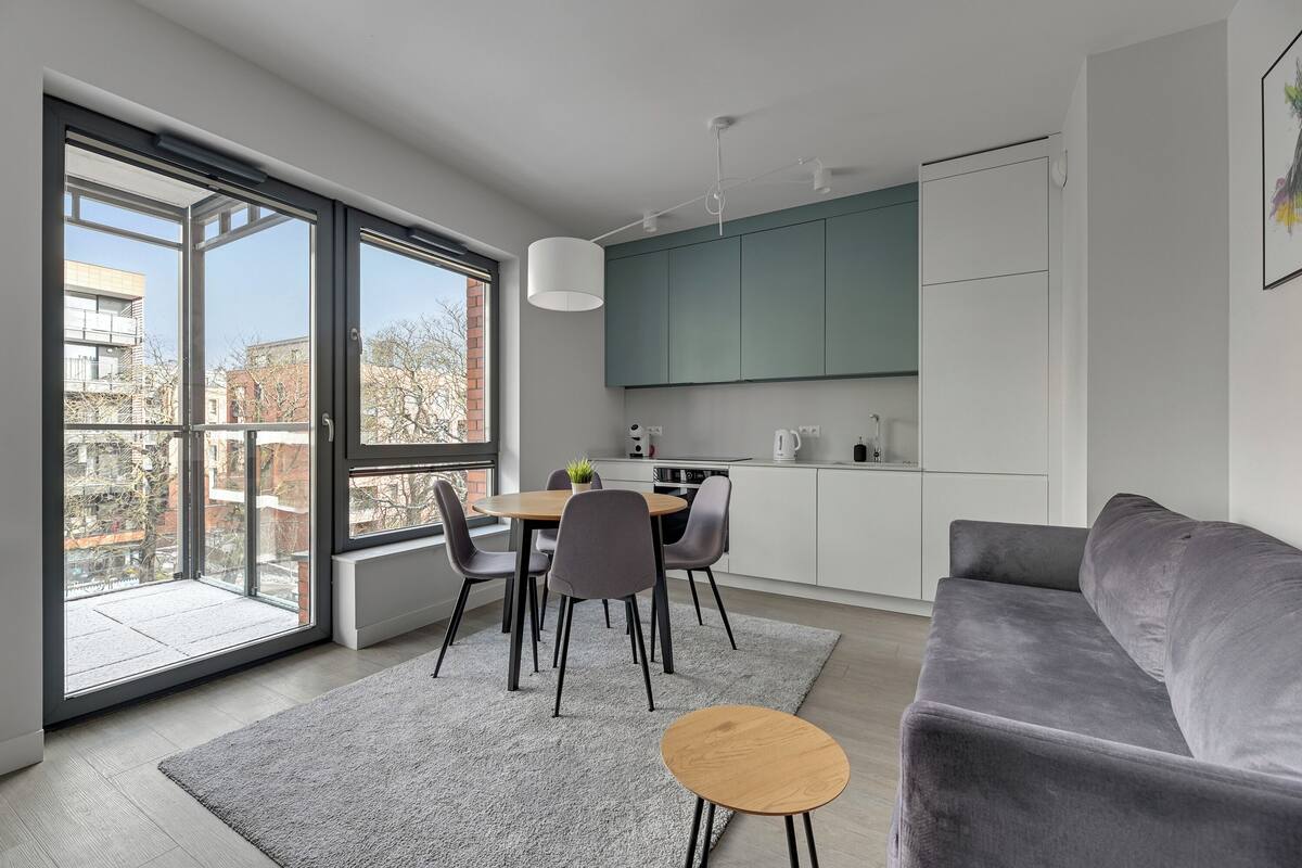 A modern apartment with a dining area, a gray sofa, and a kitchen with a green accent wall.