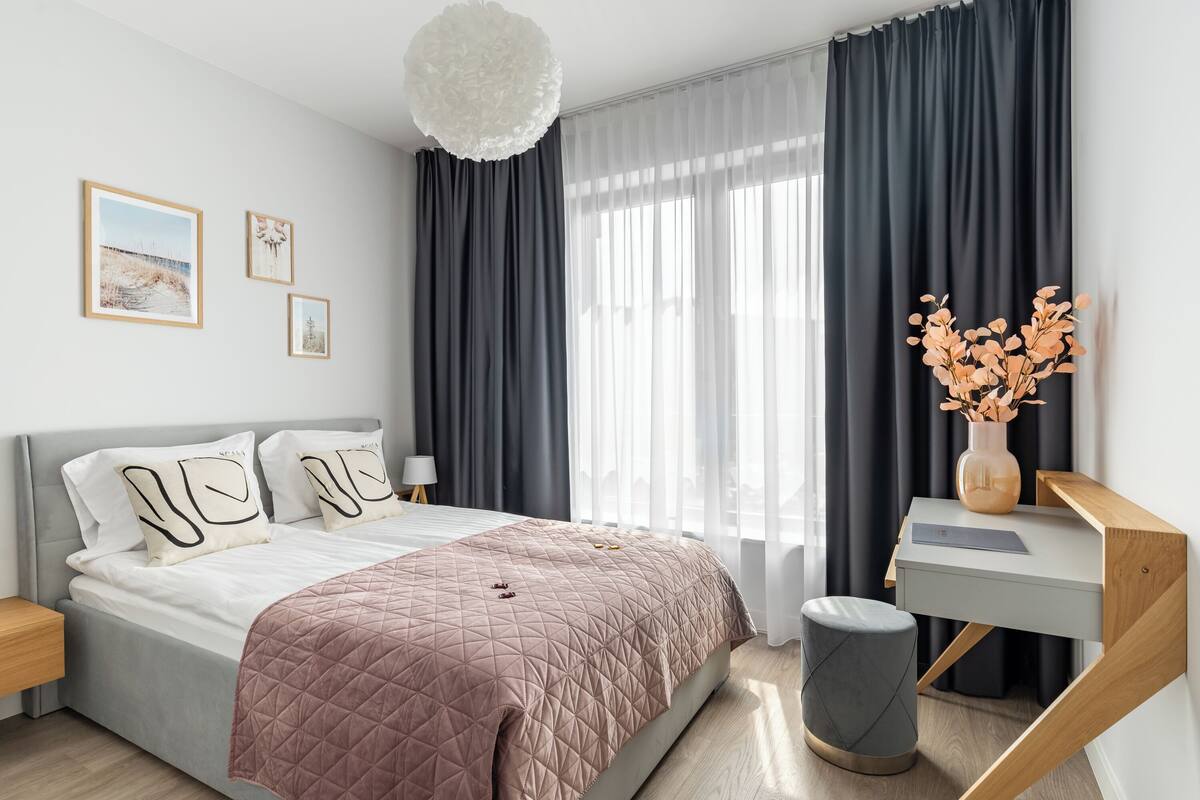 A modern bedroom with a bed, bedside tables, a desk, and a large window with curtains.