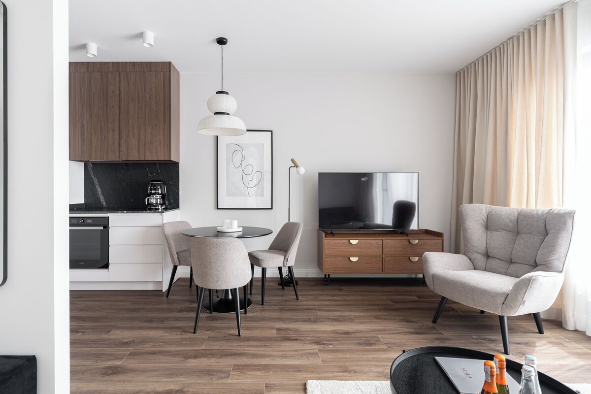 Una sala de estar moderna con un sofá, una mesa de comedor con sillas, un televisor y una zona de cocina con estufa y armarios.