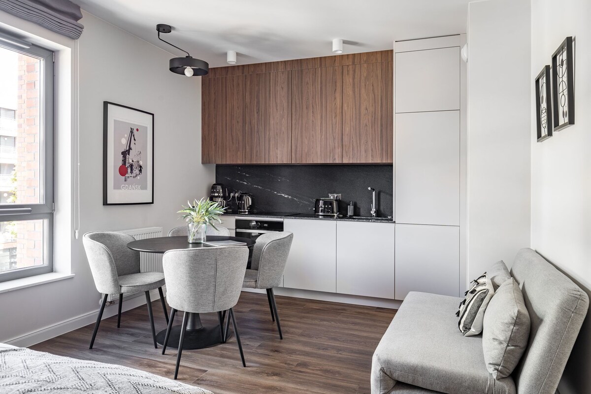 Una cocina compacta con comedor, un sofá y un ventanal con vistas a un edificio de ladrillo.