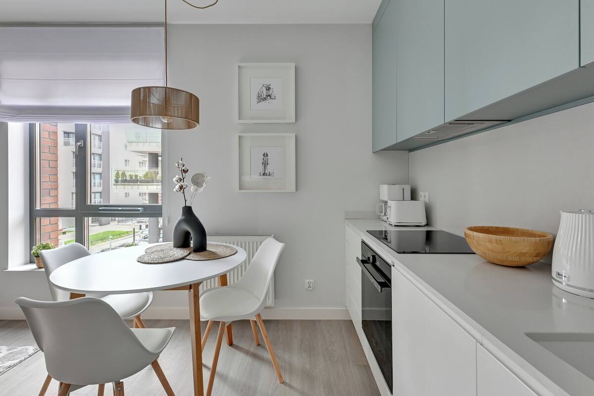 A modern kitchen with white cabinetry, a dining table with chairs, a hanging light fixture, and artwork on the wall.