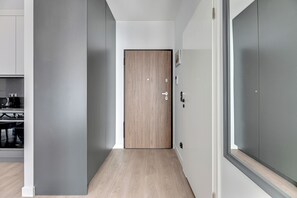 Un pasillo con una puerta de madera, una zona de cocina con electrodomésticos modernos y una pared gris.