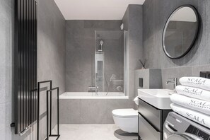 Un baño moderno con bañera, inodoro y un espejo grande.