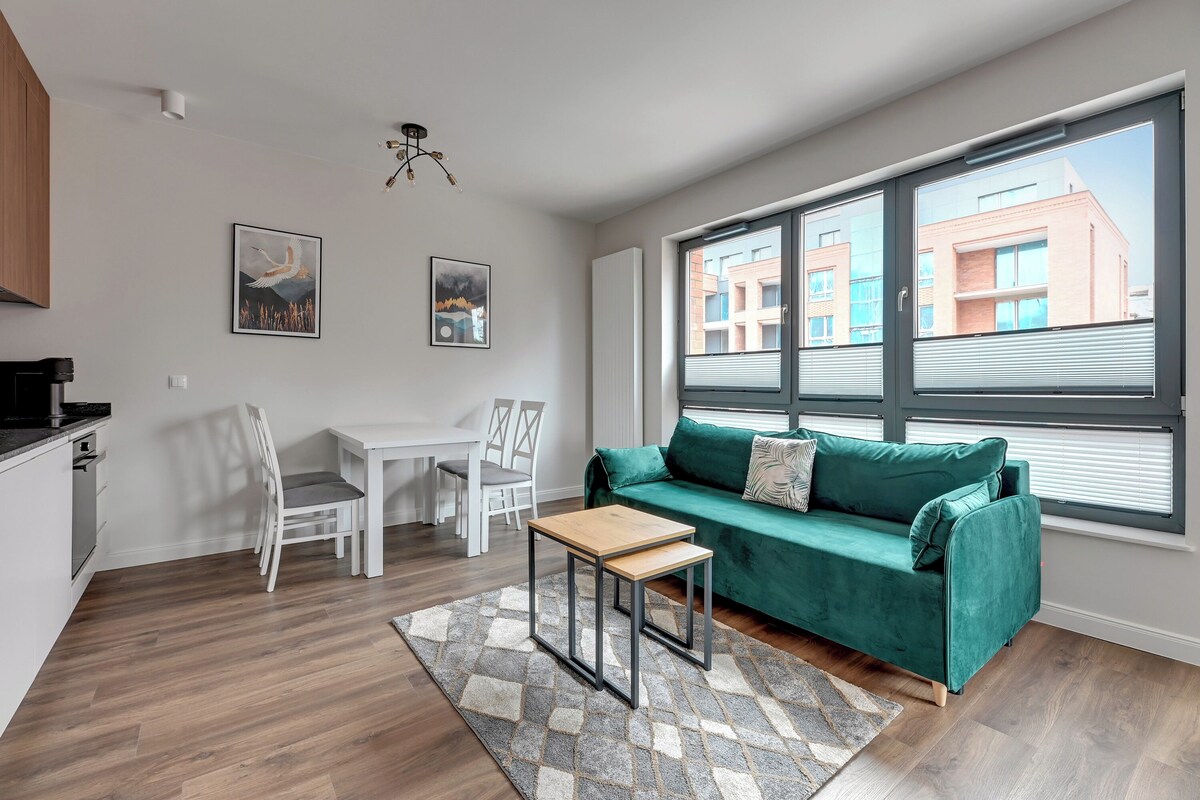 Una sala moderna con un sofá verde, una mesa de centro de madera y una zona de comedor con sillas blancas.