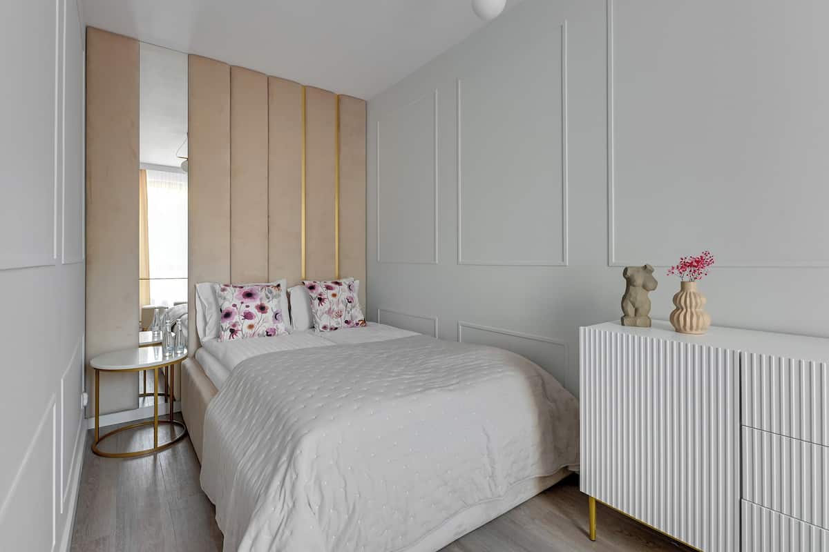 A modern bedroom with a large bed, a bedside table, a white dresser, and a mirror.