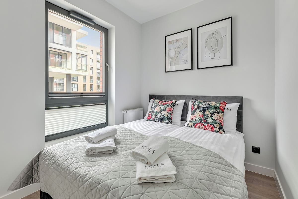 A modern bedroom with a large bed, two pillows, a quilted bedspread, and a window with blinds.