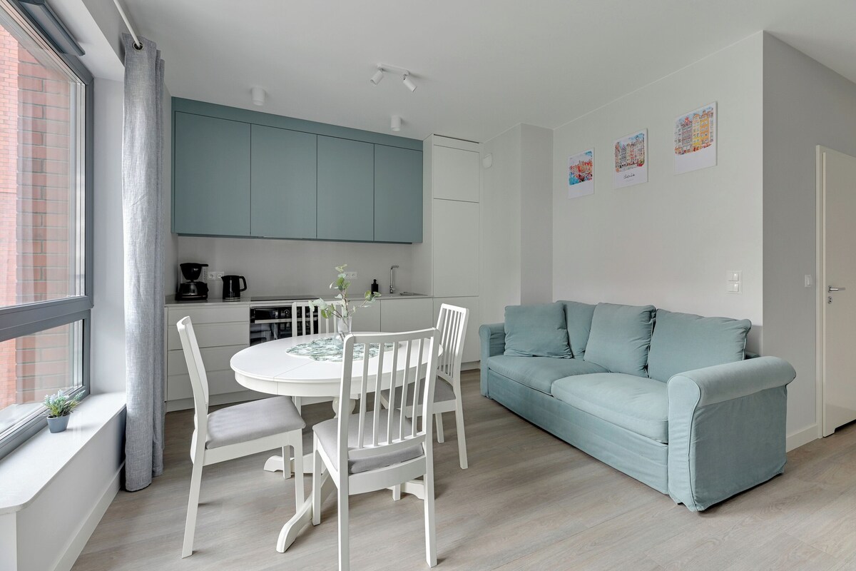 Una cocina moderna con armarios color turquesa, un comedor con sillas blancas y un sofá azul claro.