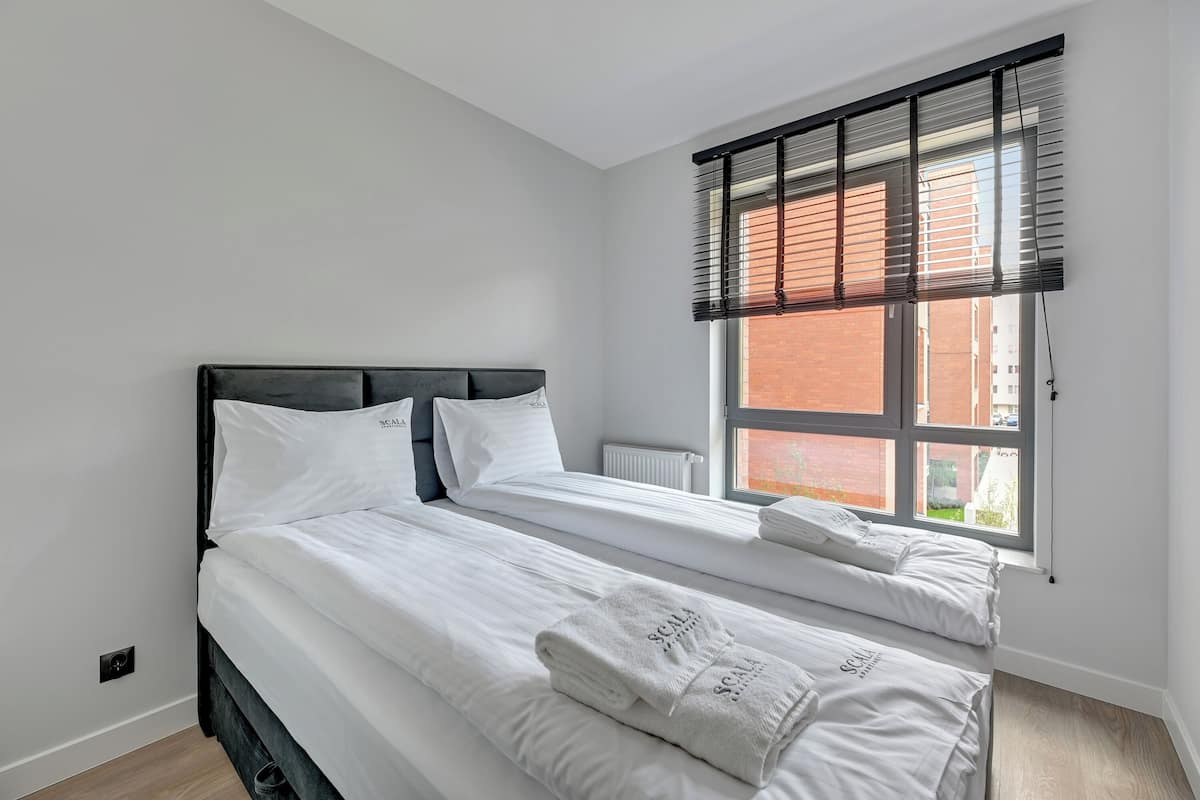 A bedroom with two beds, a window with blinds, and a radiator.