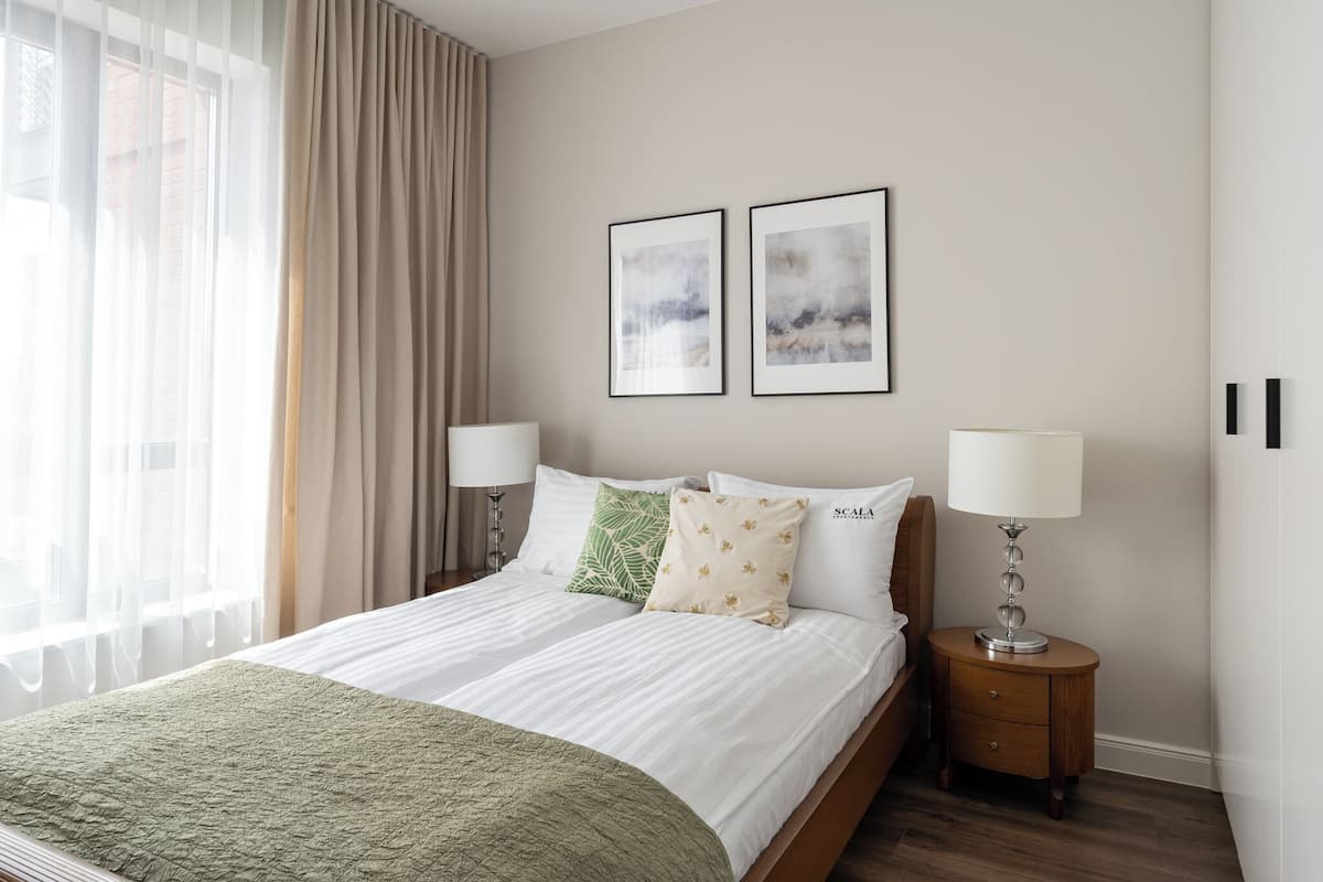 A hotel room with a bed, two bedside tables, a lamp, and two framed pictures on the wall.