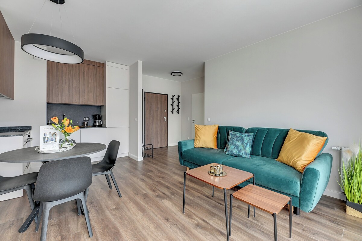 Una sala moderna con un sofá color turquesa, una mesa de centro de madera, y un comedor con una mesa redonda y sillas.