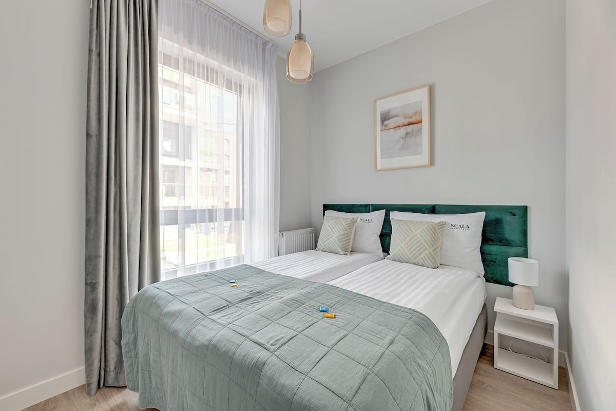 A modern bedroom with a large bed, a nightstand, and a window with sheer curtains.
