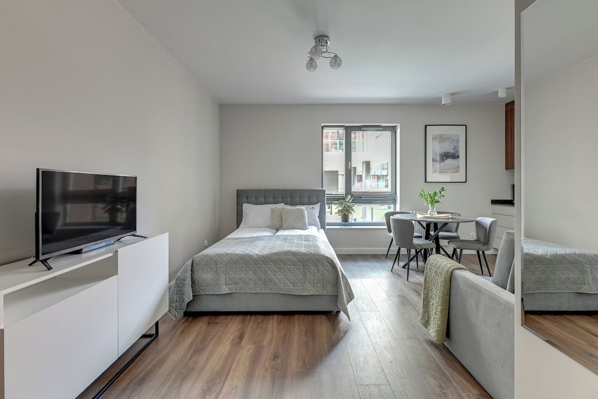 A modern bedroom with a bed, bedside table, TV, and a window with a view.
