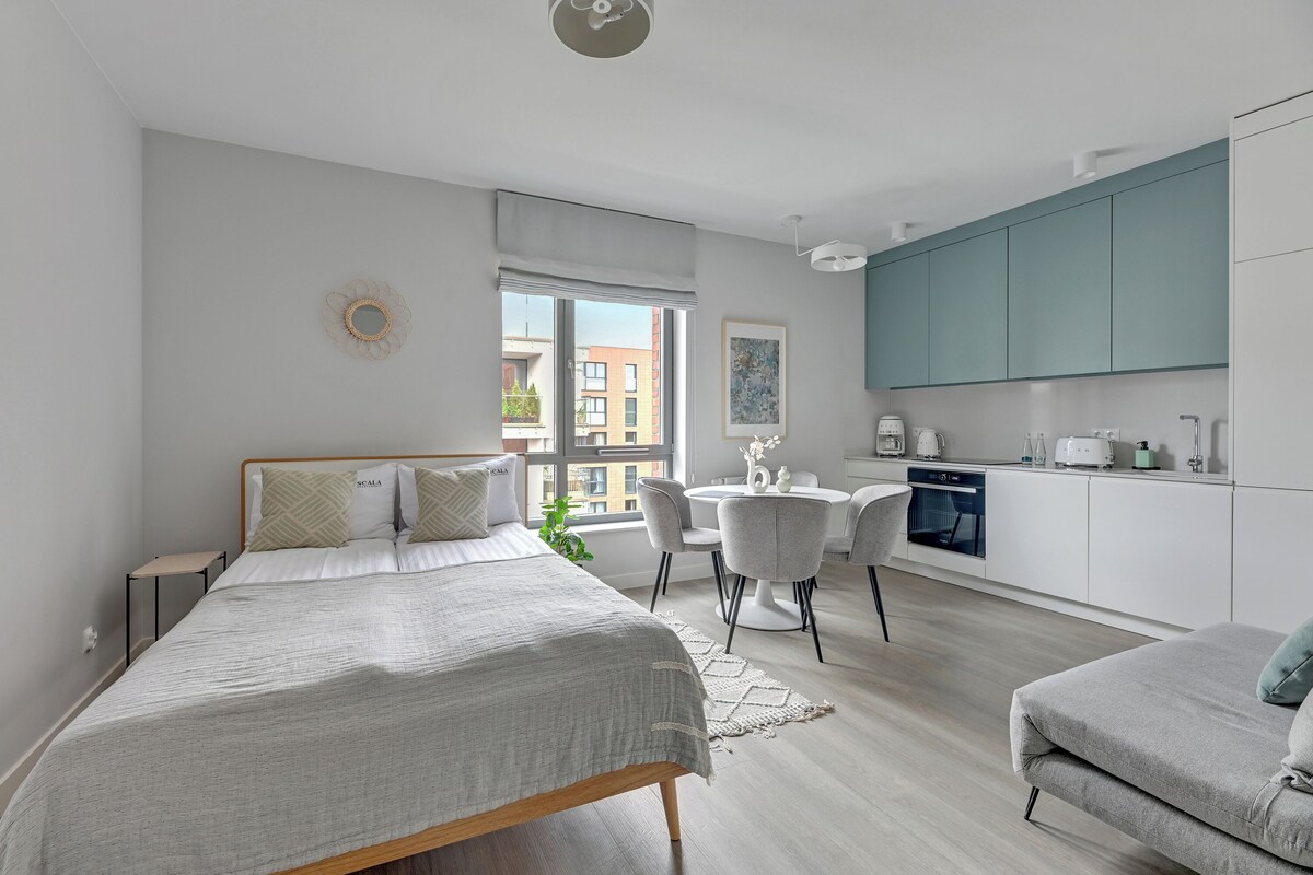 Un dormitorio moderno con una cama grande, un escritorio pequeño y una kitchenette al fondo.