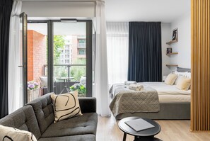 A modern hotel room with a balcony, a sofa, a bed, and a small table.