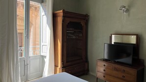 A bedroom with a bed, a wooden wardrobe, a television on a dresser, and a window with curtains. - The houses of the Piazzetta - Apartment Levanzo (Trapani)