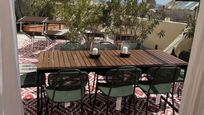 A terrace with a wooden table and chairs, patterned floor, and a view of buildings and hills. - The houses of the Piazzetta - Apartment Levanzo (Trapani)