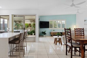Une cuisine moderne dotée d’un coin bar, d’une table à manger et de chaises, agrémentée de plantes en pot et d’un téléviseur fixé au mur.