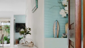 Een gang met een witte deur, een surfboard decoratie en een potplant.