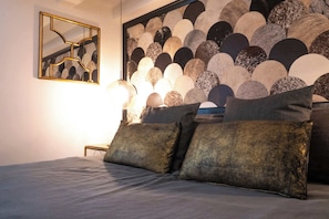Un lit avec une tête de lit ornée d’un motif géométrique, une table de chevet avec une lampe et une œuvre d’art encadrée accrochée au mur.