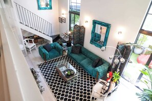 A spacious living area with a staircase, teal sofas, a coffee table, and a large mirror.