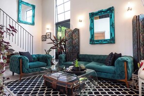 Ein geräumiges Wohnzimmer mit türkisfarbenen Sofas, einem Glastisch und einer Treppe mit Geländer.