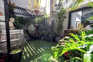 Une cour avec une statue, un tonneau en bois et diverses plantes en pot.