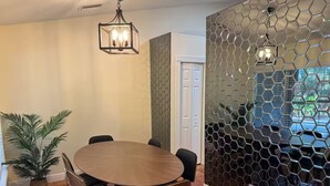 Un coin repas avec une table ronde et des chaises, une plante en pot et un mur orné d’un motif hexagonal.