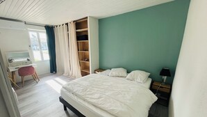 Un dormitorio con cama, escritorio, silla, armario y mesita de noche con lámpara.
