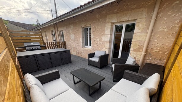 Un patio con mobiliario exterior, una parrilla y un muro de piedra.