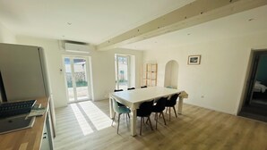 Una cocina amplia con una isla grande, un comedor con una mesa larga y sillas, y vistas al exterior a través de puertas correderas amplias.