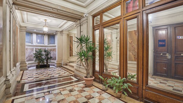 A hallway with a checkered marble floor, large potted plants, and a wooden door with a sign. - Luxurious AC apartment Saint Honoré (Paris)