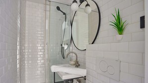 A modern bathroom with a glass-enclosed shower, a white sink with a towel, a mirror, and a potted plant. - Superb Suite in Neuilly Porte Maillot (Neuilly-sur-Seine)