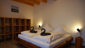 Un lit en bois avec une literie blanche et deux oreillers en forme de cygne, une table de chevet en bois avec une lampe, et une étagère en bois.