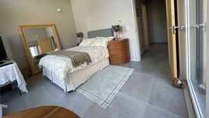 Un dormitorio con cama, mesita de noche, lámpara y espejo, con vistas al pasillo.