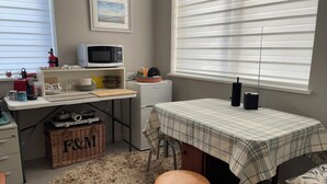 Una cocina compacta con microondas, tostadora y refrigerador pequeño. Hay una cesta de mimbre debajo del mostrador y un mantel escocés sobre un taburete.