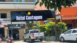 A hotel named Hotel Contagem with a prominent sign, a white pickup truck parked in front, and a motorcycle parked nearby. - Hotel Contagem (Sobradinho II)