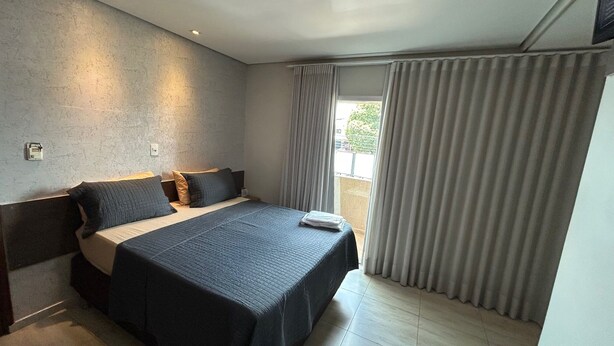 A modern hotel room with a large bed, a nightstand, and a window with curtains. - Hotel Contagem (Sobradinho II)