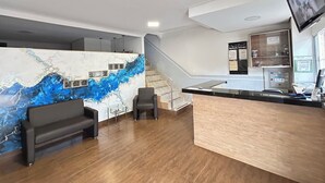 A reception area with a marble wall, a reception desk, a staircase, and a mounted TV. - Hotel Contagem (Sobradinho II)