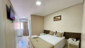 A hotel room with a large bed, a bedside table with a phone and a lamp, a TV mounted on the wall, and a window with curtains. - Hotel Contagem (Sobradinho II)