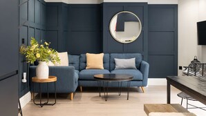 Een moderne woonkamer met een donkerblauwe modulaire bank, een ronde spiegel en een kleine ronde tafel.