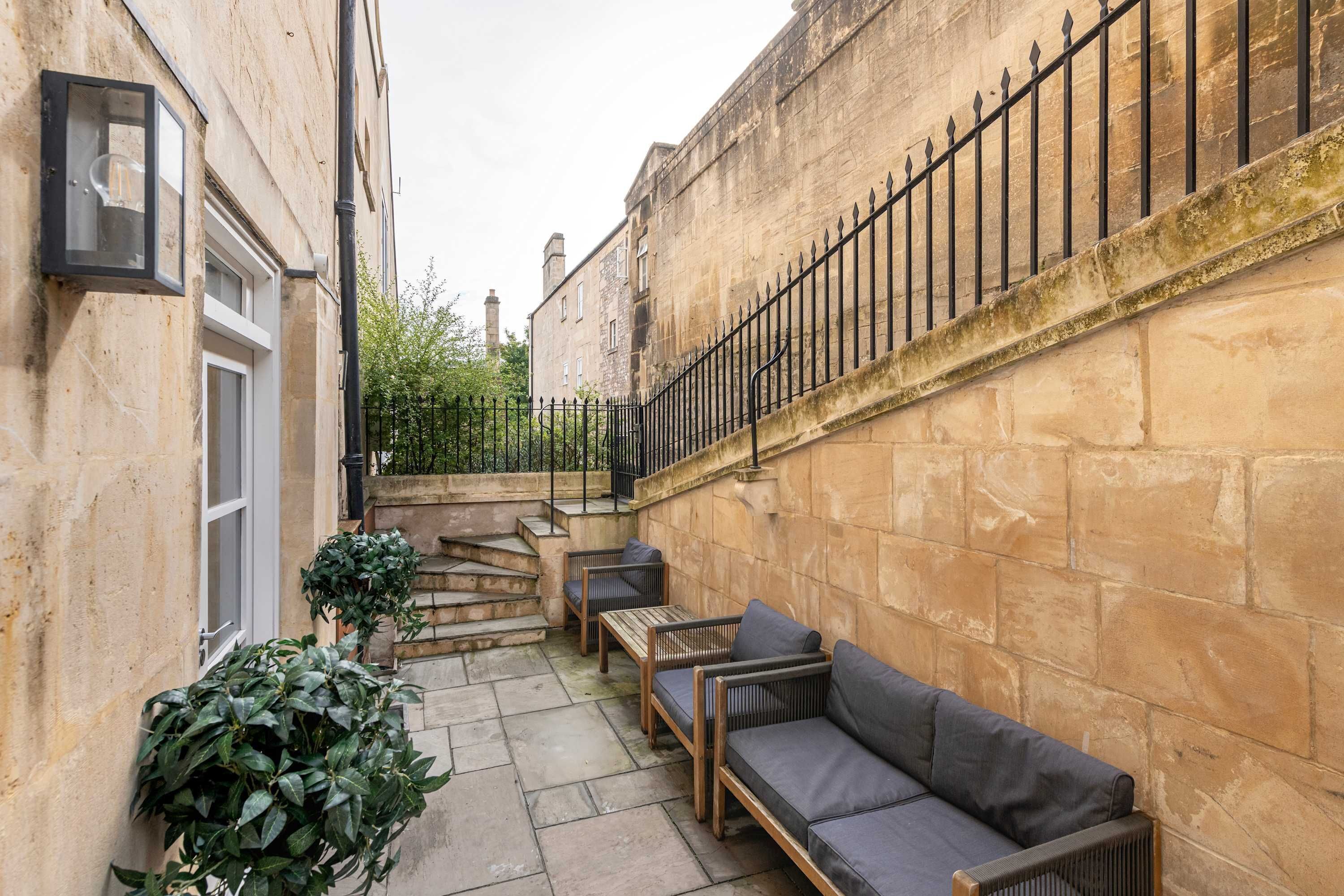 A courtyard with stone walls, a black metal fence, and outdoor seating.