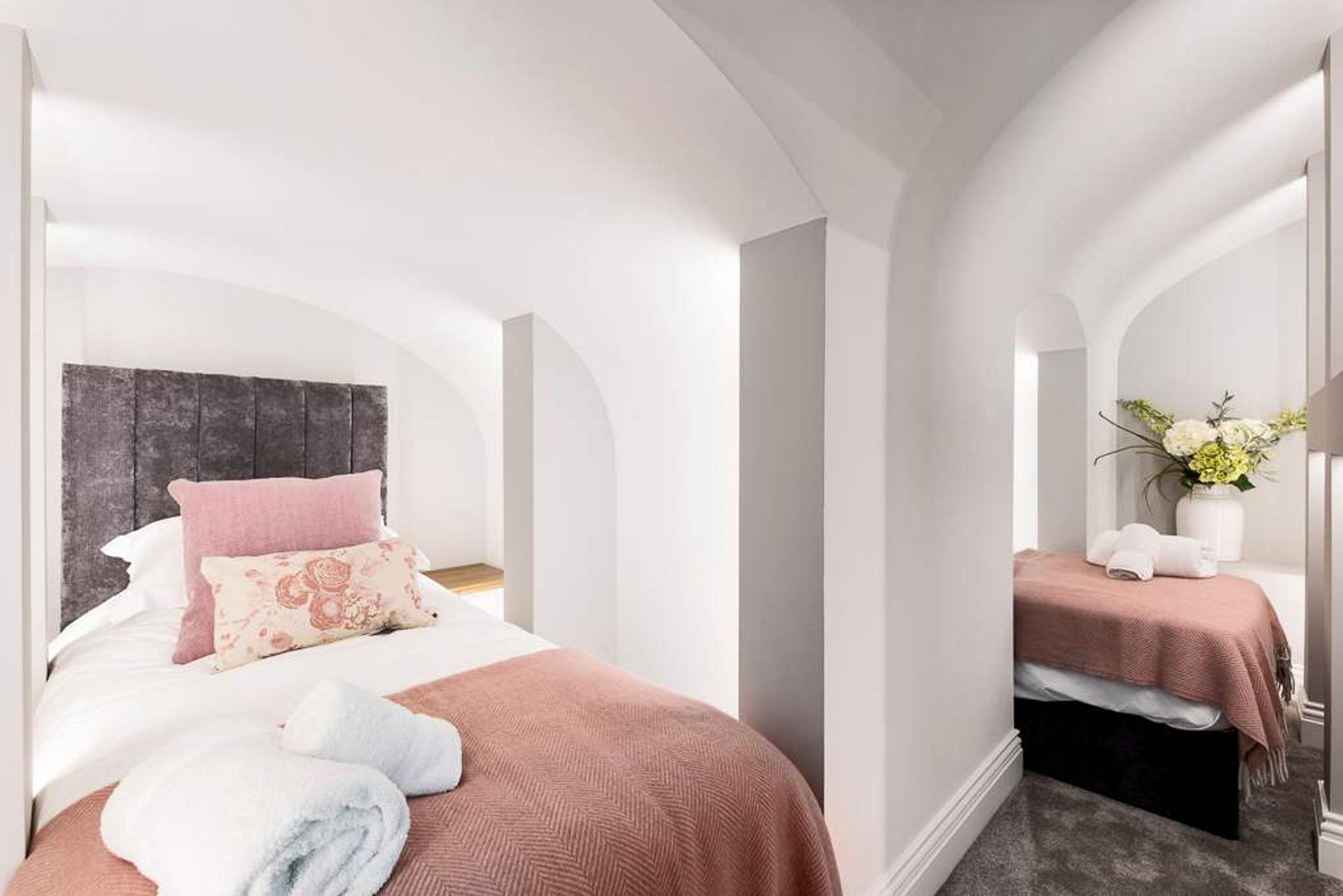 A hotel room with a large bed, a smaller bed, and a bench. There is a vase with flowers on the bench.